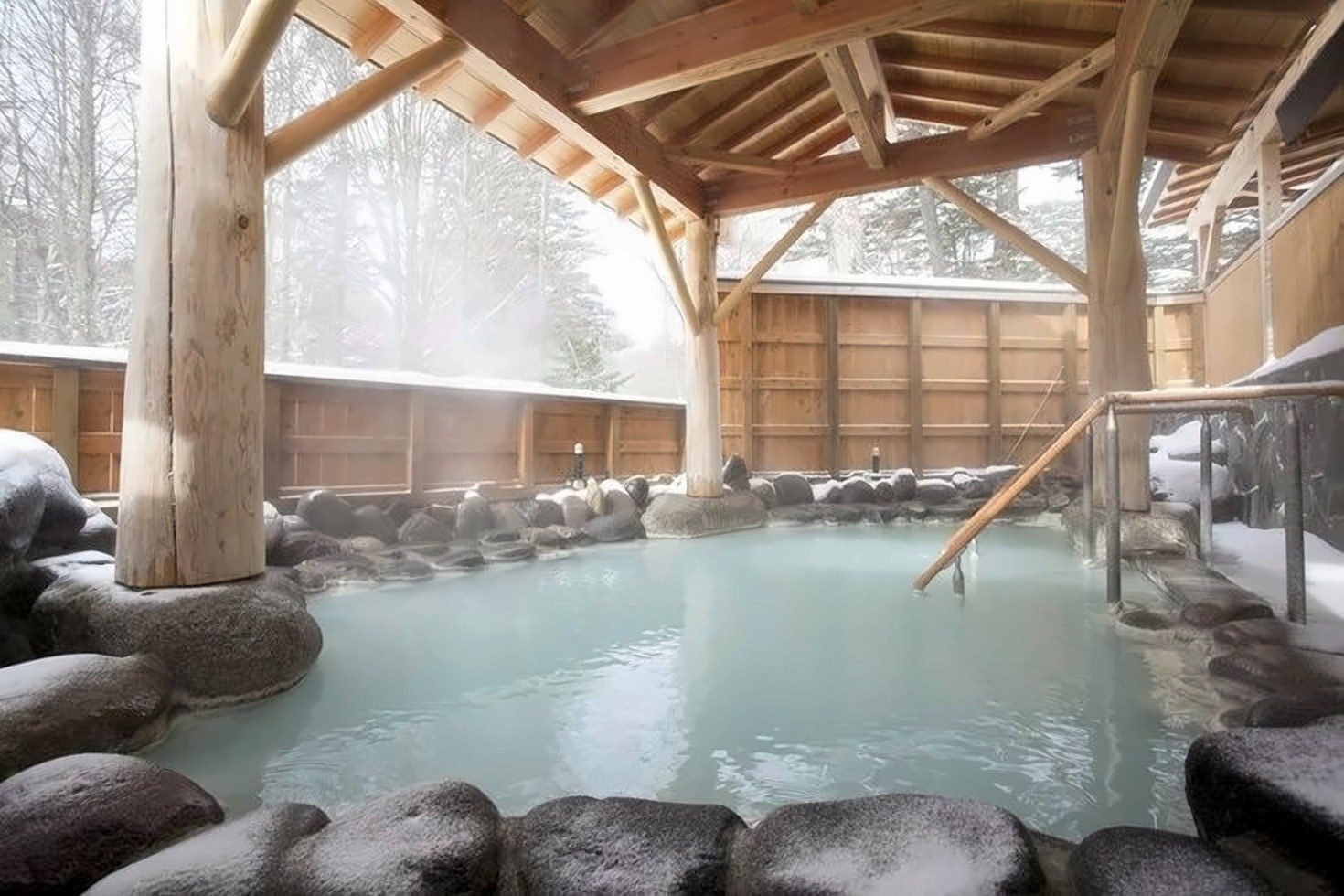 Bain onsen en plein air, bordé de rochers et de bois, en hiver